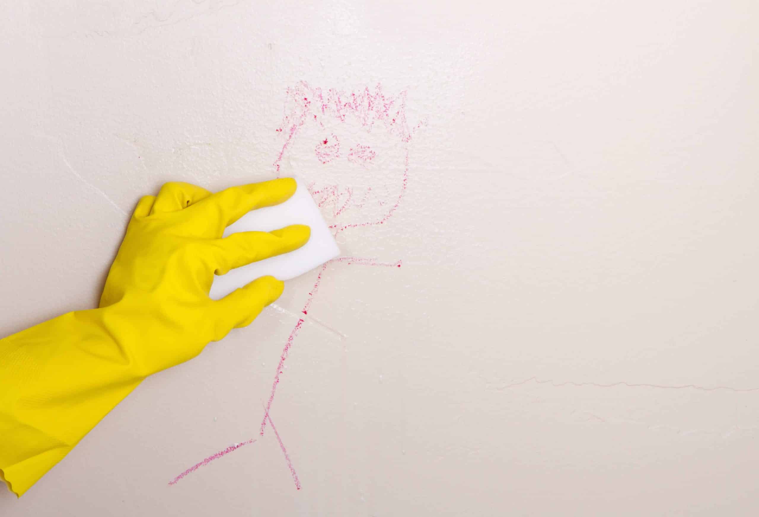 Person with yellow rubber glove cleaning drawing on wall