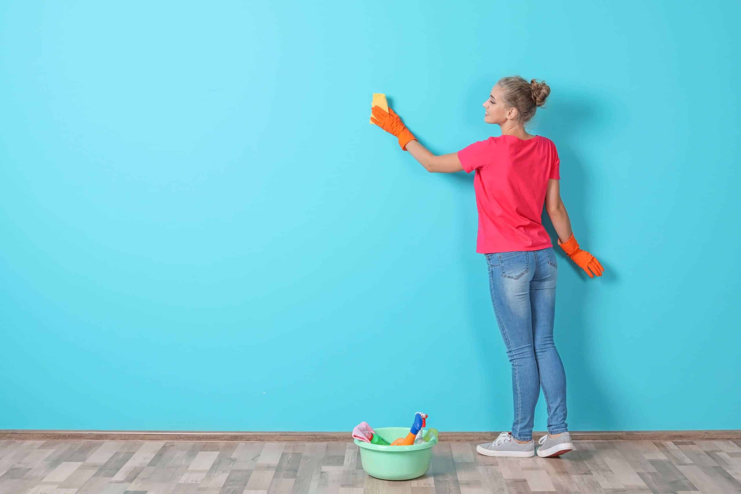 Woman in red t-shirt facing a blue wall cleaning it.
