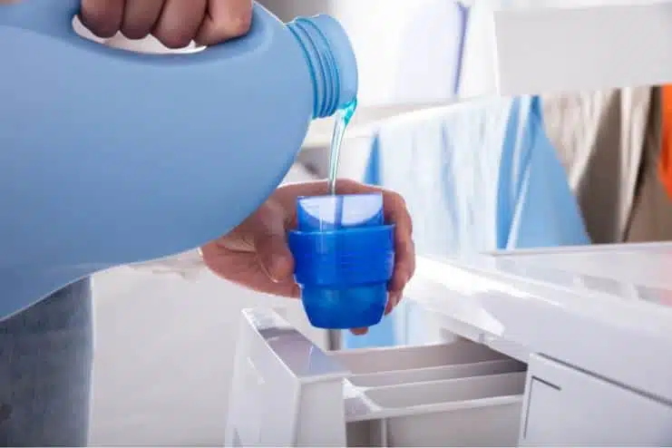 man standing in front of a front loader washing machine pouring blue laundry detergent into detergent lid