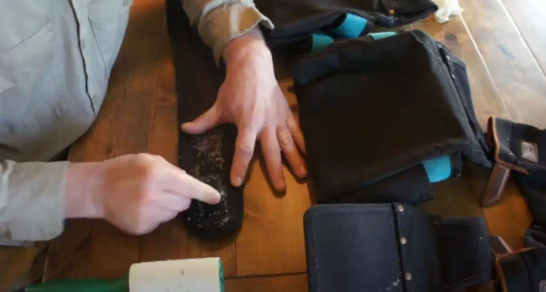 man using lint roller to clean velcro bag strap on a wooden desk