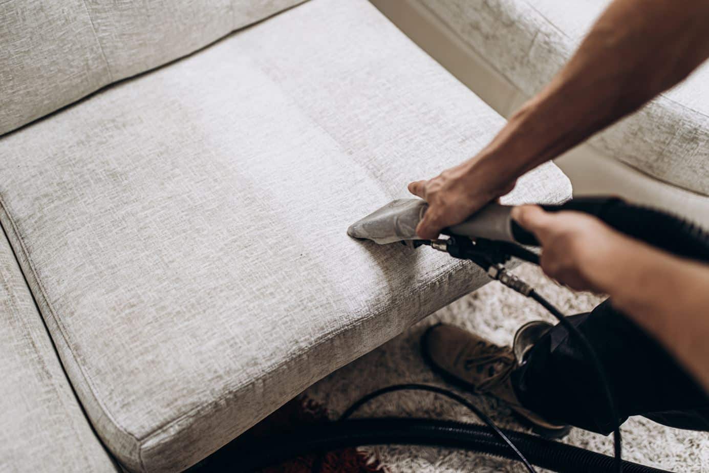 man using steam cleaning to deep clean a grey upholstered couch
