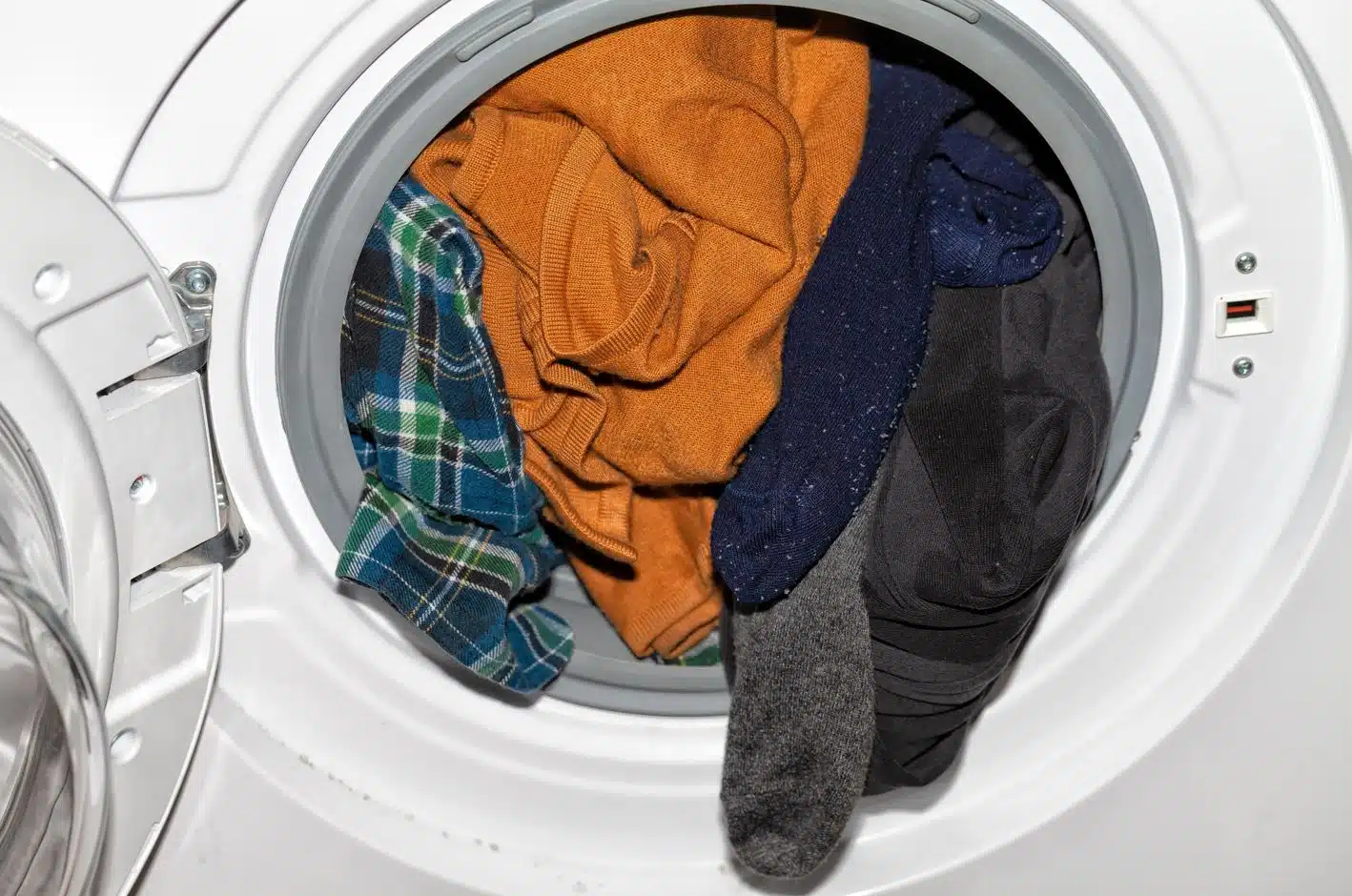 front view of a white front load washing machine overloaded with clothes with its door open