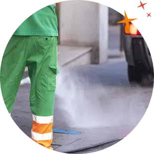 Jun wearing green overalls using high pressure to clean a dirty concrete footpath