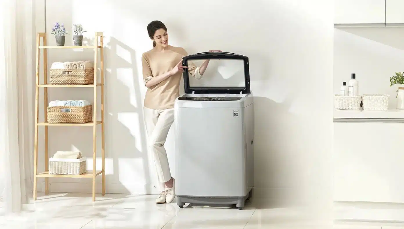 woman opening lid of large top loader washing machine in a minimalist laundry